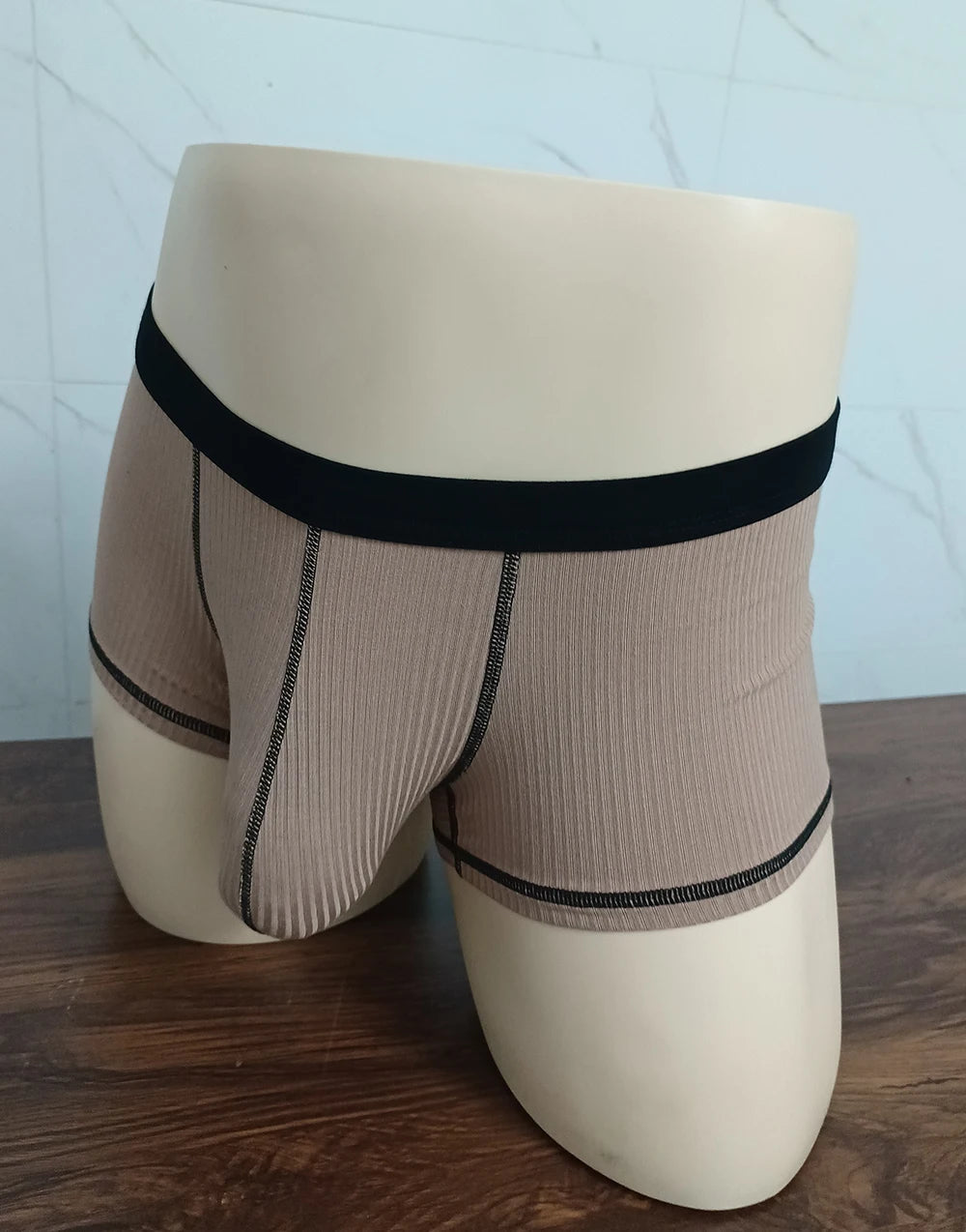 Beige boxer shorts on a mannequin with wide black waistband and contrast trim, front pouch