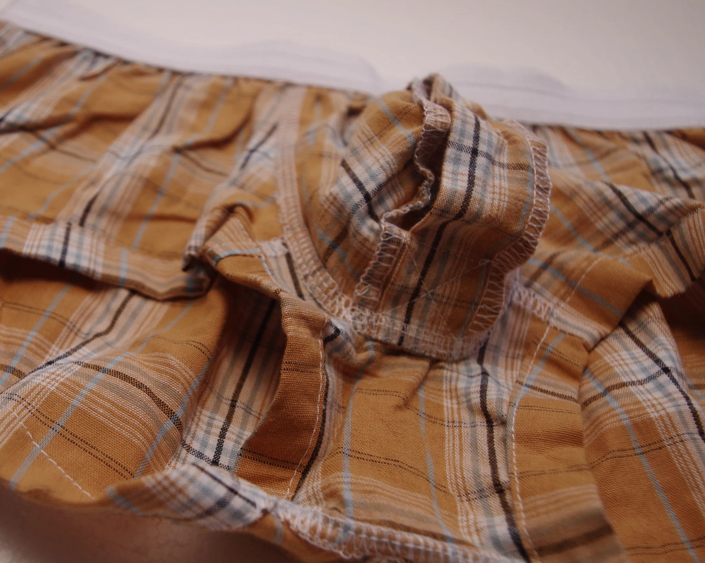 Plaid cotton boxer brief fabric close-up, tan/orange plaid with blue and white stripes