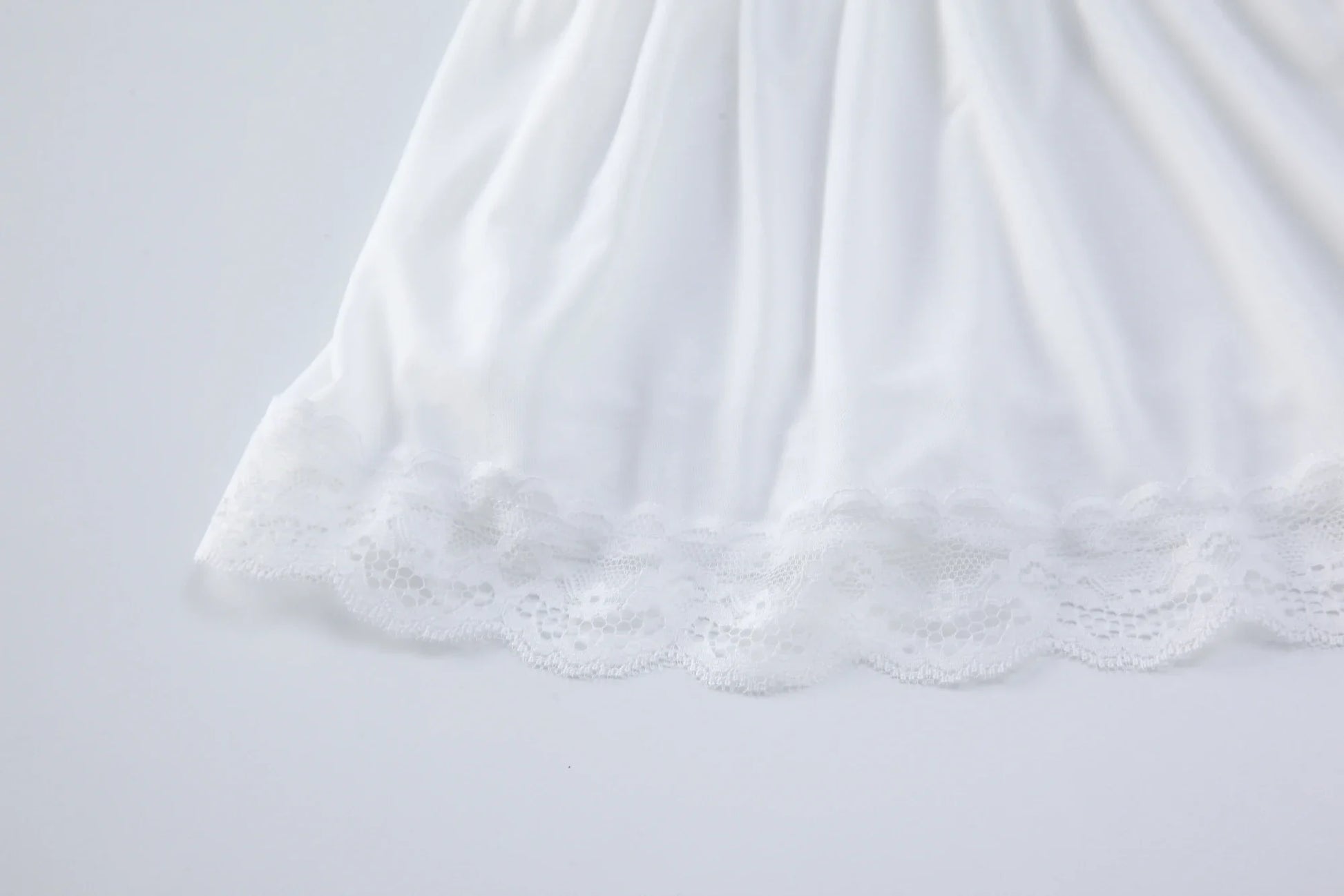 White babydoll bodysuit skirt with lace trim hem and soft, flowing ruffle layers