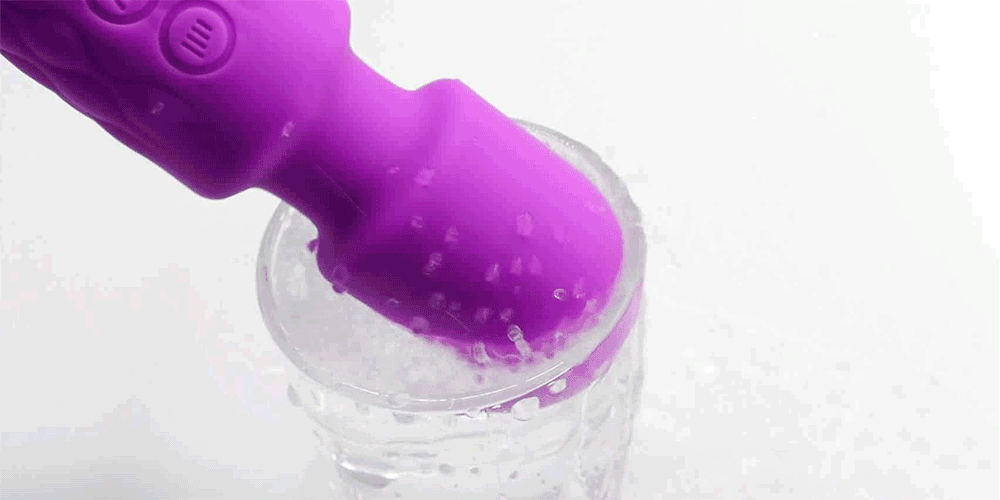 Purple magic wand vibrator tip held near clear bowl-style container, textured handle and buttons