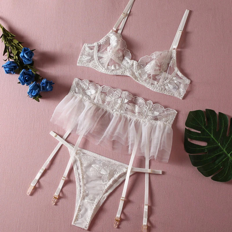 White embroidered mesh lingerie set laid flat: bra, tulle ruffle briefs, and garter straps.