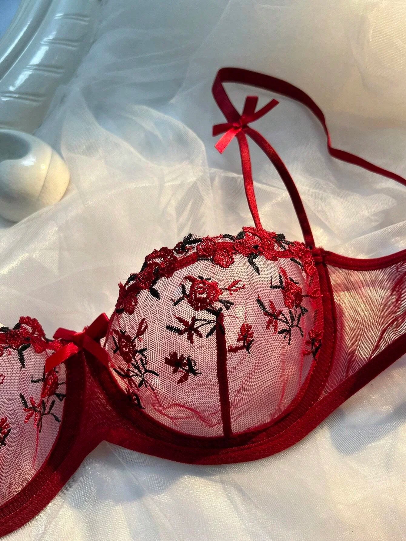Red sheer lace bra cup close-up with floral embroidery and bow strap